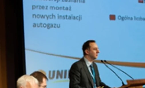 Rzecznik w formalnym stroju i płaszczu wygłasza przemówienie podczas wydarzenia, korzystając z sprzętu audio i mikrofonu. Tekst na obrazie podaje całkowitą liczbę konwersji na LPG w 2012 roku.